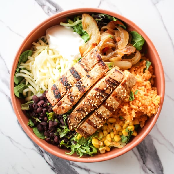 Overhead view of a colorful chicken fajita bowl with rice, beans, corn, cheese, and sour cream.