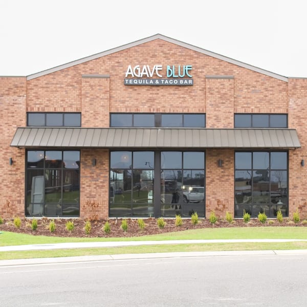 Exterior of Agave Blue Tequila & Taco Bar, a brick building with large windows and a metal awning.
