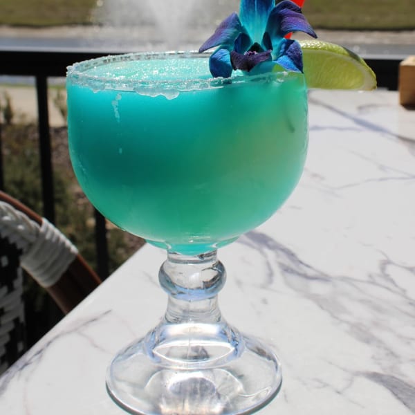 A vibrant blue frozen drink, garnished with a blue orchid and lime, sits on a marble table.
