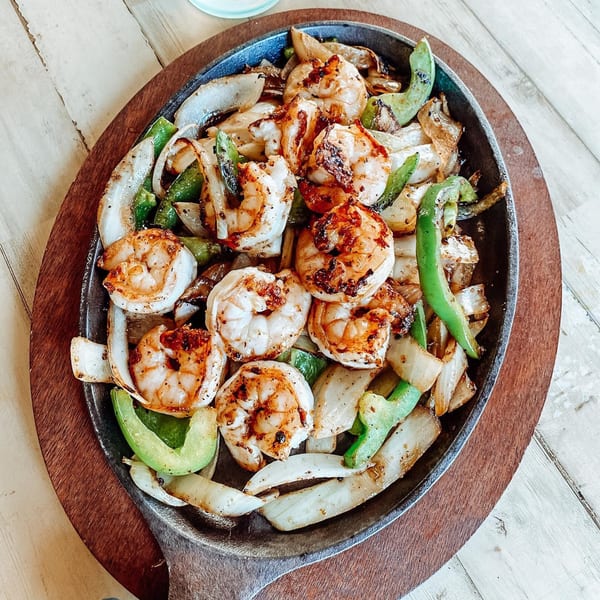 Sizzling shrimp fajitas with grilled onions and green bell peppers on a cast iron skillet.