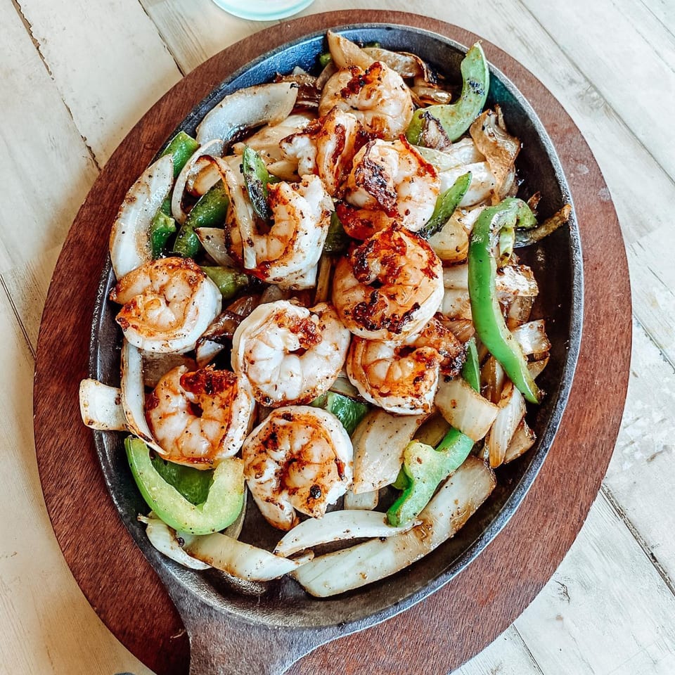 Sizzling shrimp fajitas with grilled onions and green bell peppers on a cast iron skillet.
