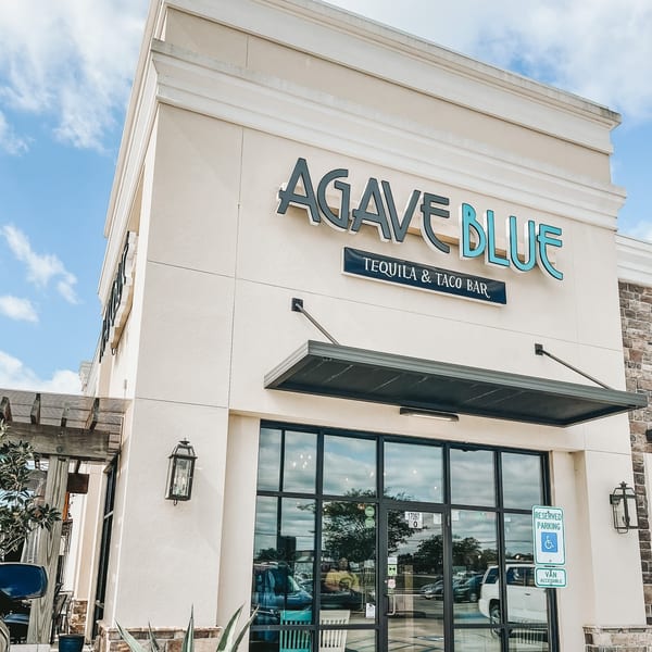 Exterior of Agave Blue Tequila & Taco Bar, a restaurant with a light-colored facade and large windows.