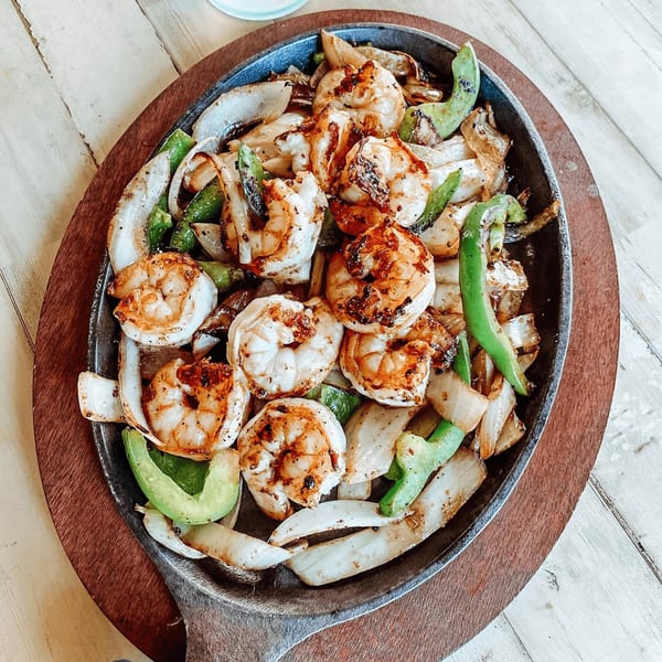 Sizzling shrimp fajitas with onions and green peppers in a cast iron skillet on a wooden board.