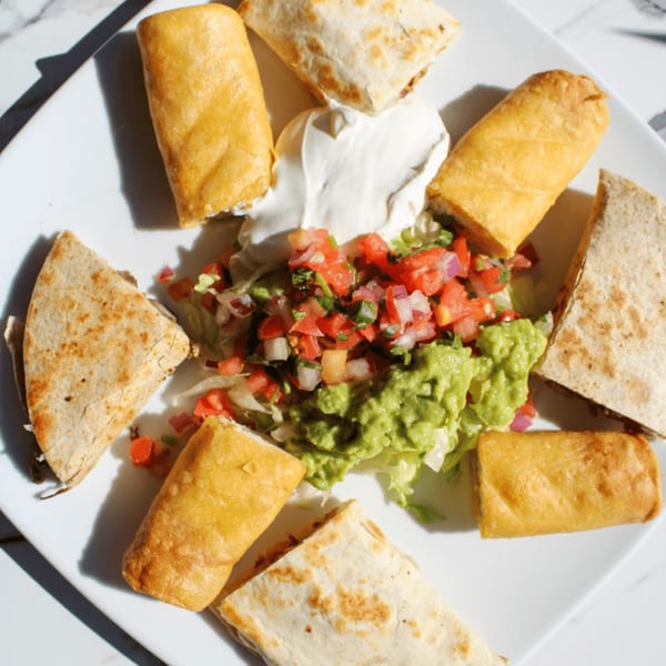 A white plate with taquitos, quesadilla wedges, guacamole, pico de gallo, and sour cream.